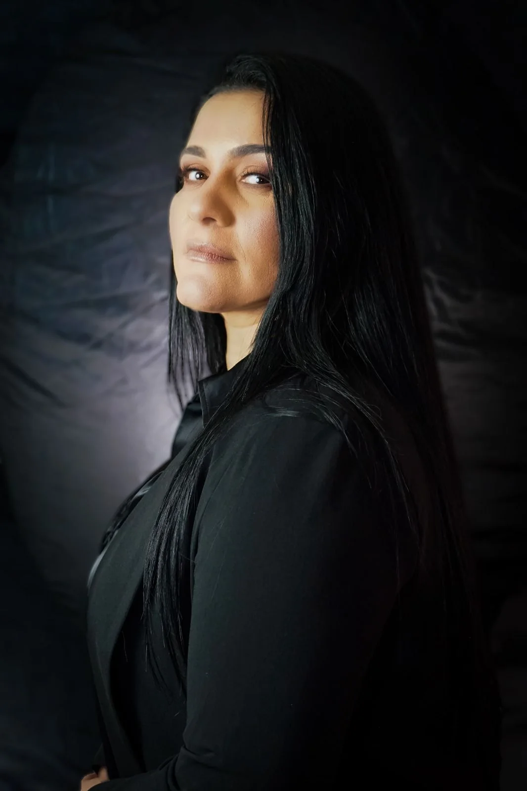 Retrato de Célia Castelo de perfil, de roupa preta, olhando pra câmera sobre fundo escuro